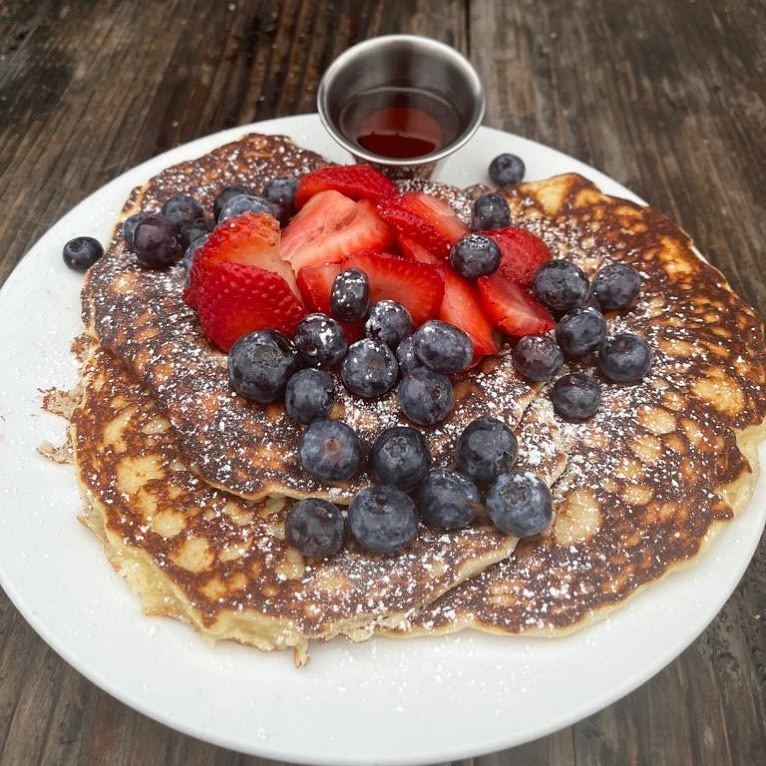 A tall stack of pancakes topped with strawberries, blueberries and syrup at Picazo Café