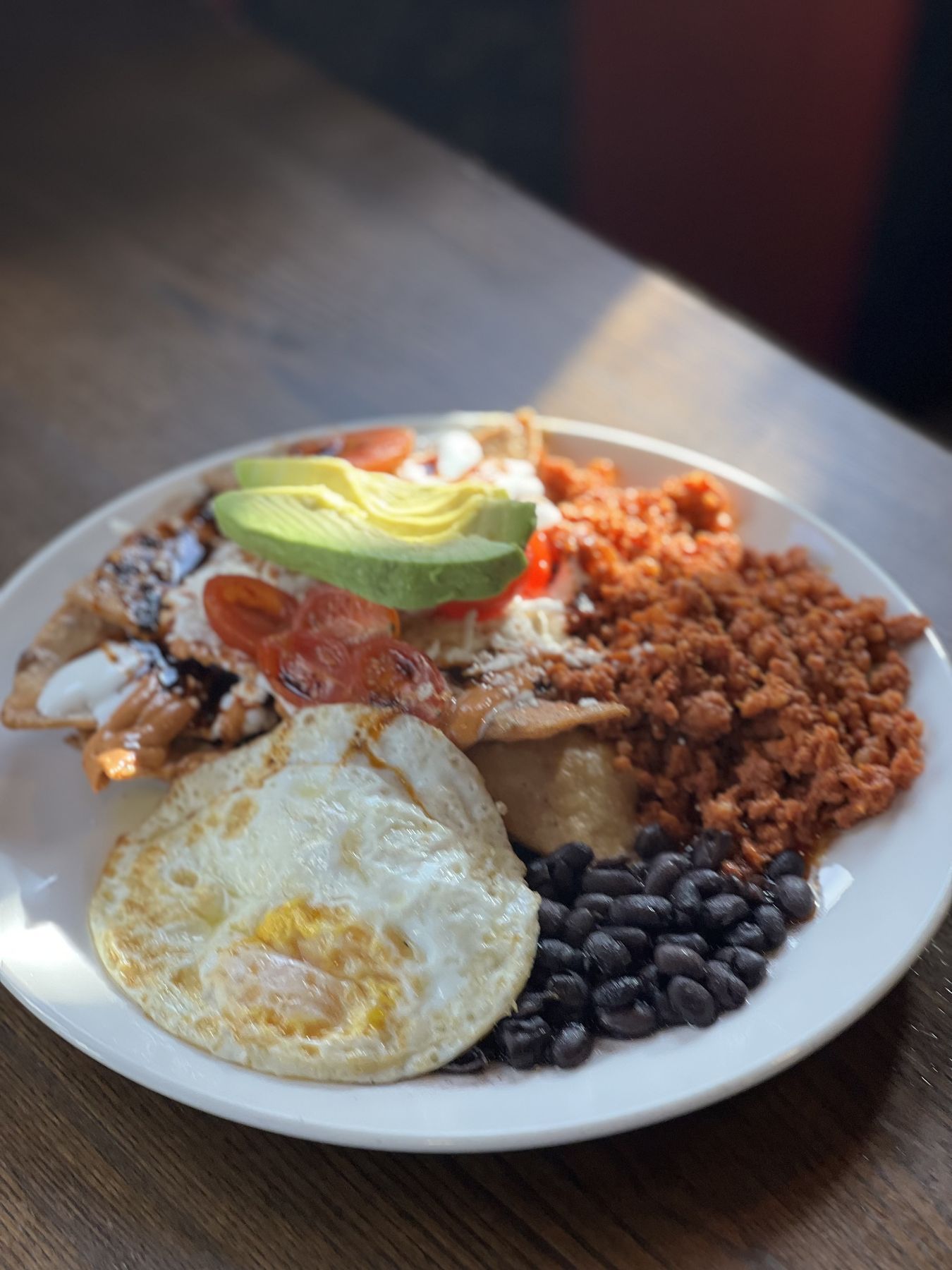 A plate of Picazo's chilaquiles topped with a fried egg, sliced avocado and cherry tomatoes, served with black beans and chorizo