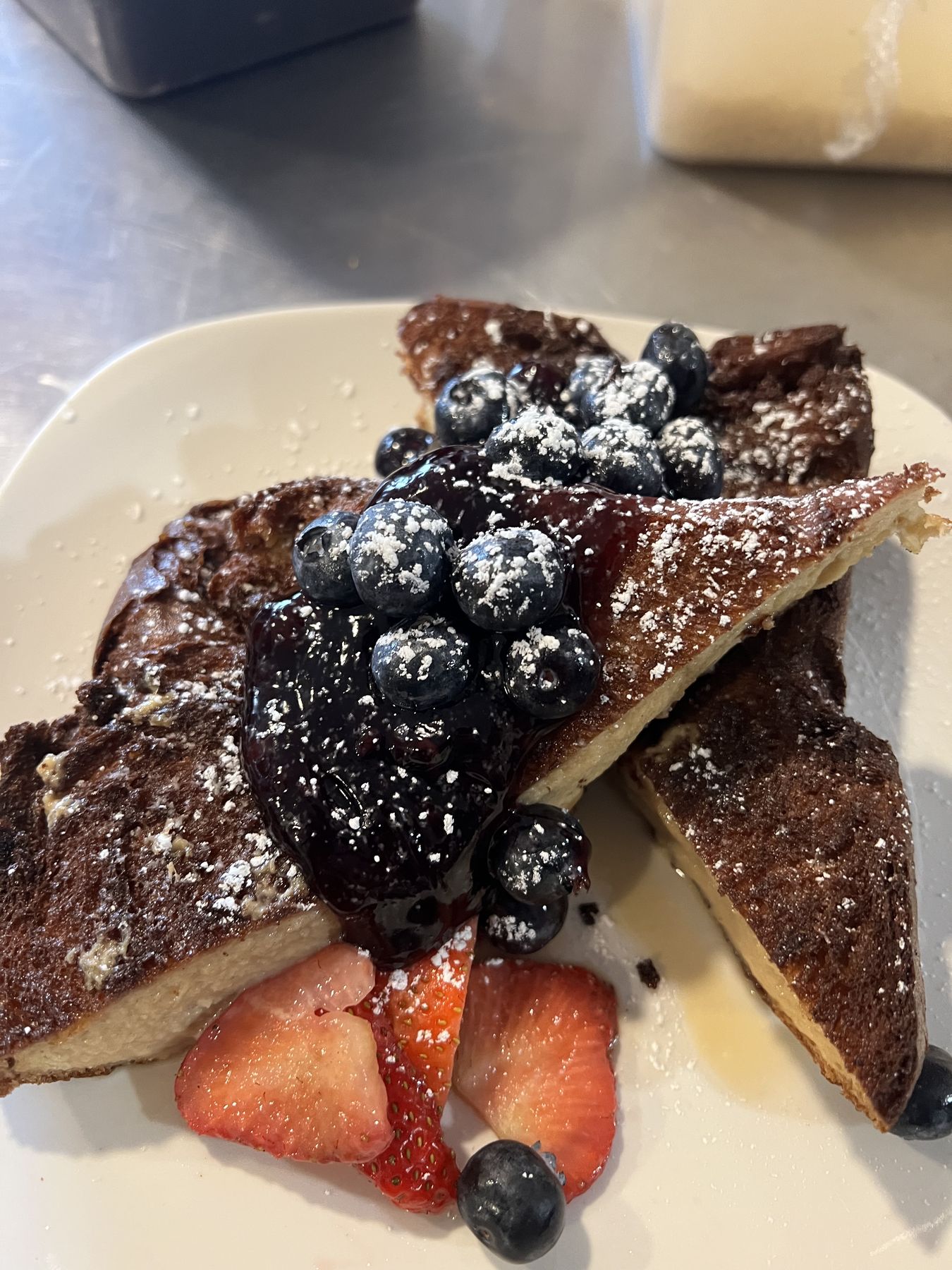 Flan French Toast dusted with powdered sugar and topped with blueberries and strawberries
